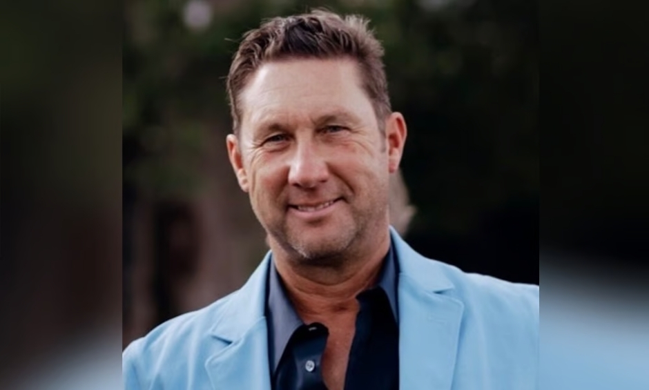Professional headshot of male white light blue suit jacket and dark blue button down shirt, natural blurred background