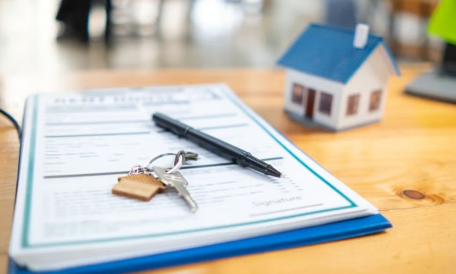 Stack of papers on clipboard with house keys and pen sitting on top, on a desk with a house