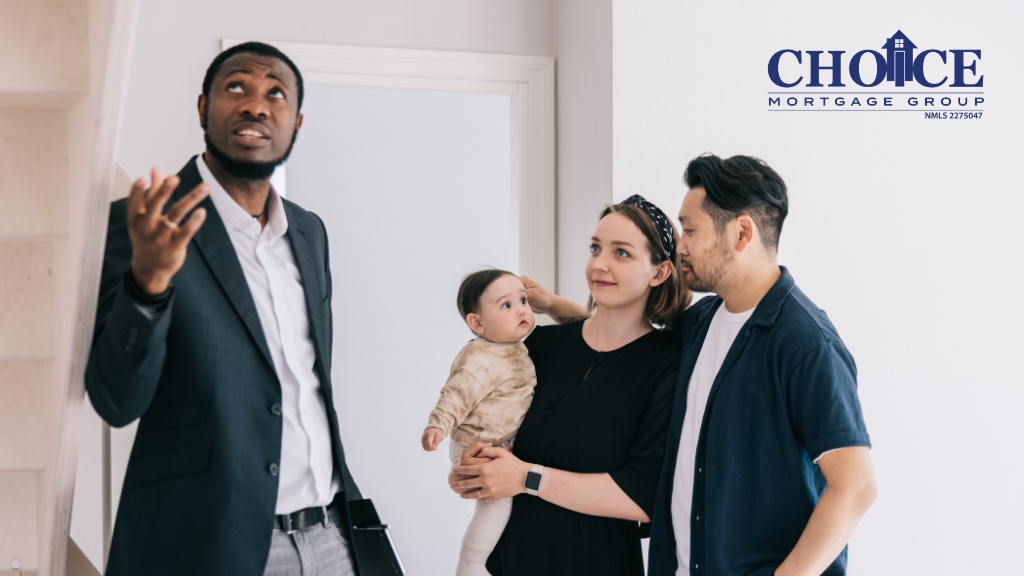 Male Realtor in dress clothes and dark jacket showing a home to a family of three, women in black shirt, man in white shirt and black jacket, and baby.
